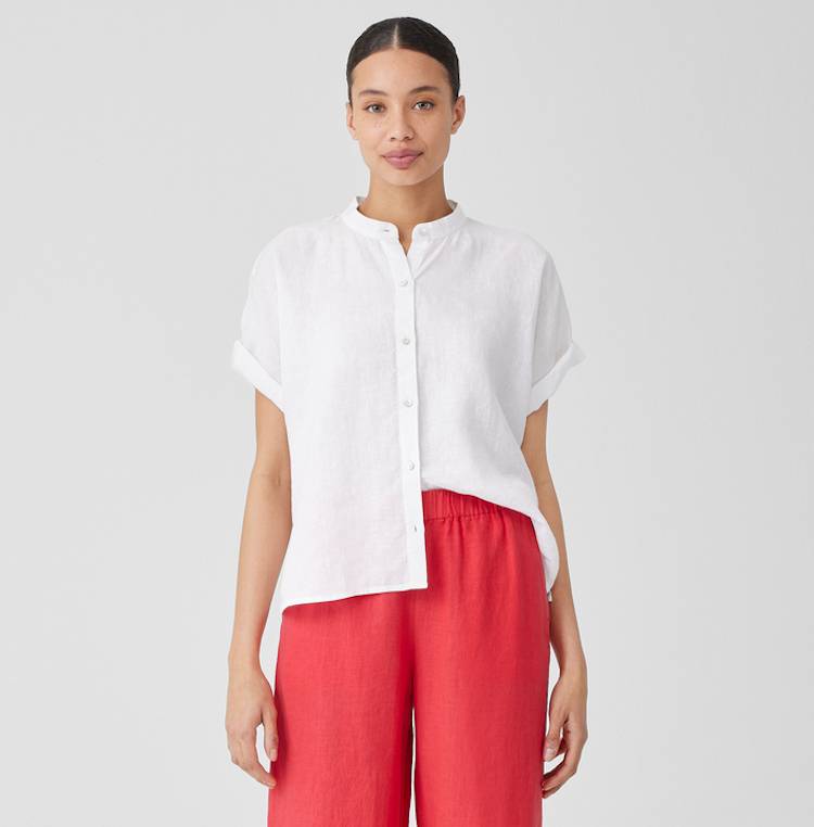 Woman in red linen pants and white linen shirt looks at camera.