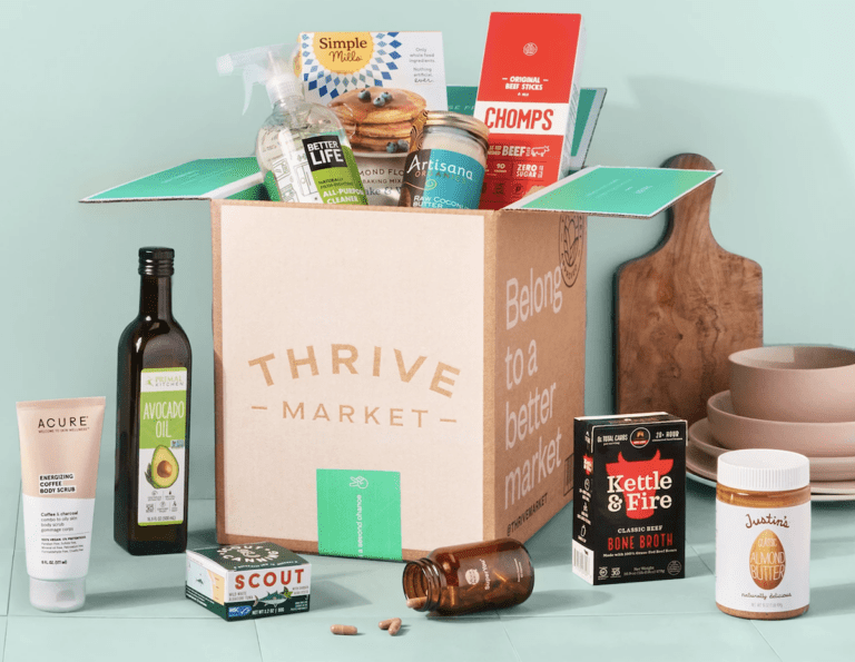 A cardboard box labeled Thrive Market, with non-perishable snacks and groceries in and around it