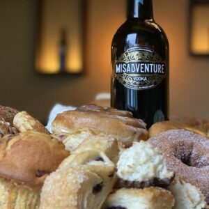 A bottle of Misadventure & Co vodka, which is made from pastries and baked goods, surrounded by pastries and baked goods.