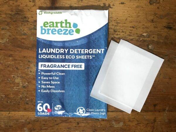 A package of Earth Breeze Liquidless Eco Sheets laundry detergent on a weathered wooden surface, with two laundry detergent sheets on display outside the package.