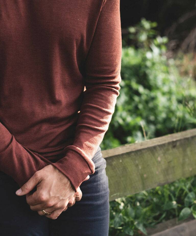A man wears a rust-colored, long-sleeved merino wool shirt from Nui.