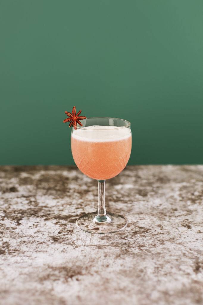 A soft pink Seedlip non-alcoholic cocktail in a decorative glass with a star anise balanced on the rim