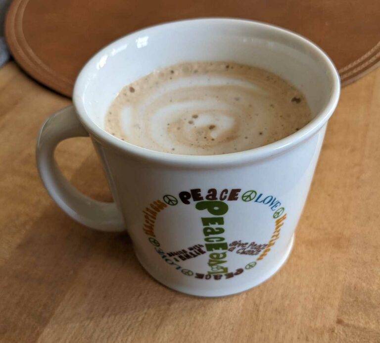 A mug with a peace sign contains a latte with foamed plant milk in an attractive swirl pattern. The plant milk is made by Joi. photo credit Julia Cooper.
