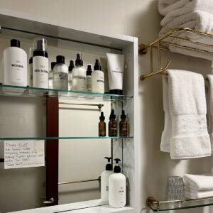 An open, mirrored bathroom cabinet with shelves stocked with toiletries from Public Goods.