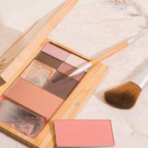 On a marble surface is an open, used bamboo Capsule Palette from Elate Beauty. It contains different shades of powder blush, eyeshadow, and eyeliner. A large face brush and small eyeshadow brush lie near the palette, which can be refilled with products of the consumer's choosing. Photo credit - Elate Beauty