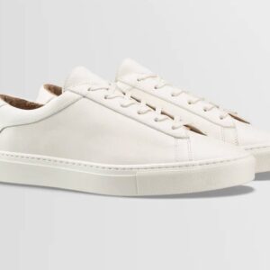 A pair of sleek, creamy white tennis shoes with white outsoles and white laces made by Italian brand Koio.