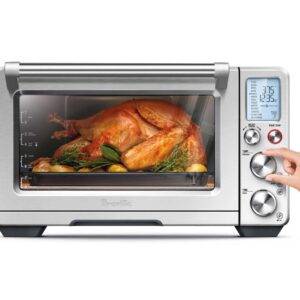 A large toaster oven made by Breville had a Thanksgiving turkey inside of it, with a woman's hand adjusting one of the knobs.