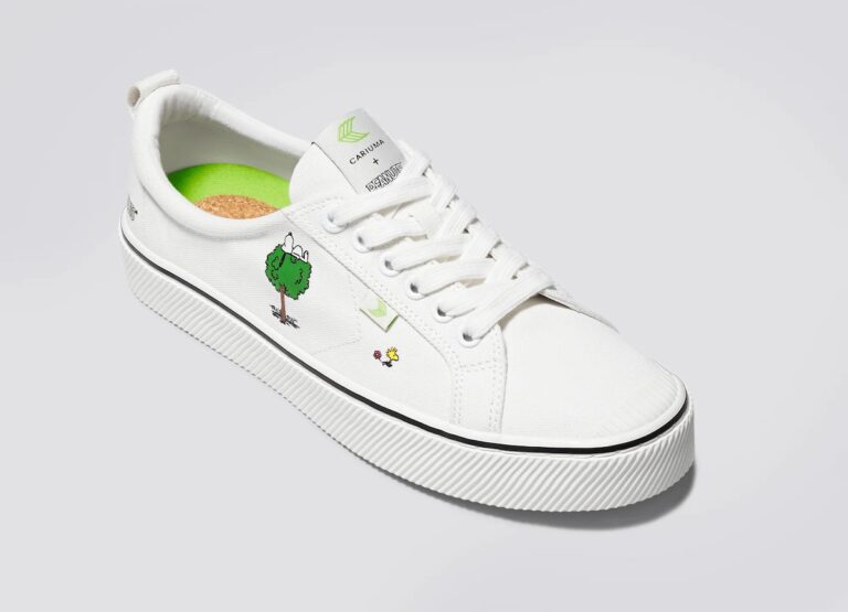 White sneakers with an illustrated tree and Charlie Brown's pet dog Snoopy on them, made by the brand Cariuma in collaboration with Peanuts. 