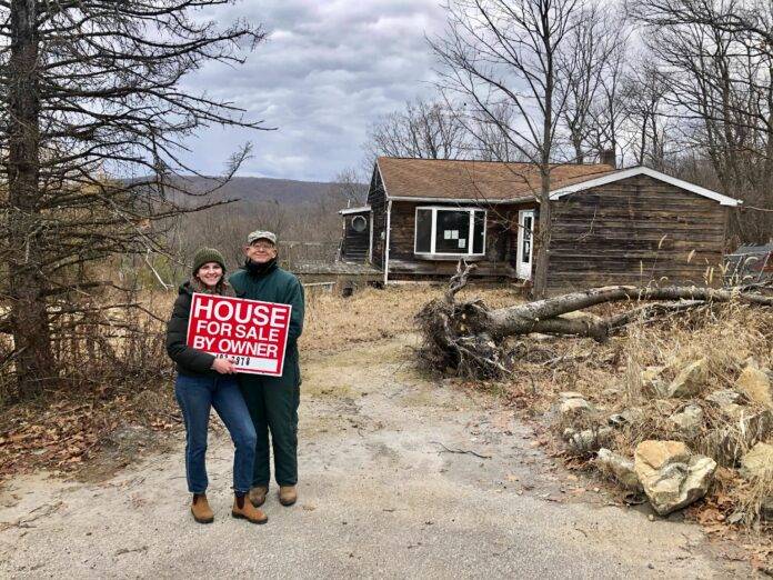 Bea Copeland stands in front of her newly purchased home holding the "for sale" sign.
