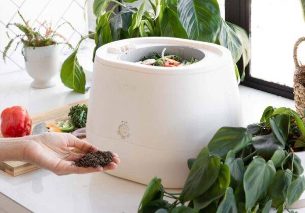 The Lomi Composter sits open on a kitchen counter, surrounded by piles of food.