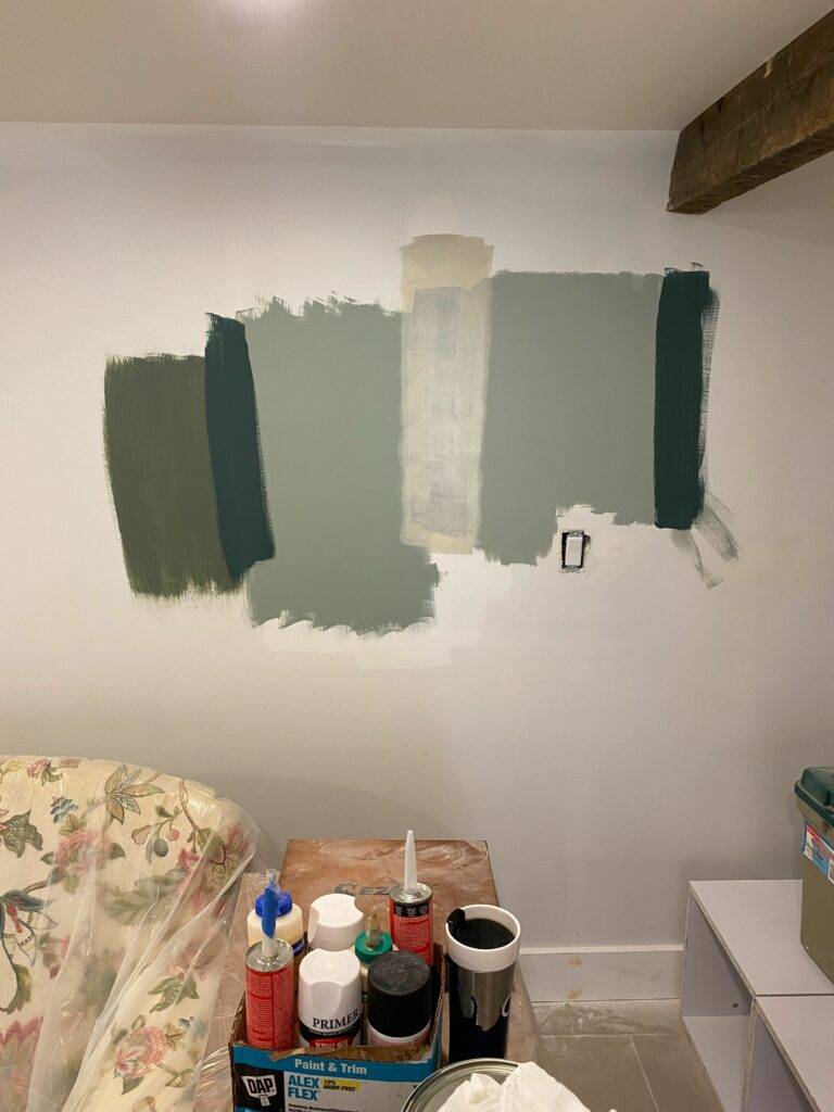 An otherwise blank wall has patches painted with various shades of cool toned blues and greens.