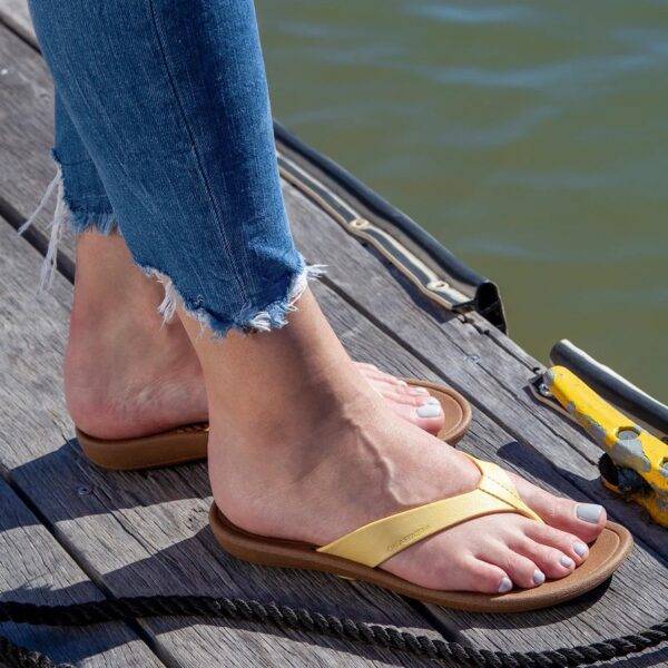 A woman's feet in brown flip flops with yellow uppers, standing on a dock.