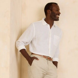 A relaxed-looking man smiles, wearing a pair of khaki trousers and a cream-colored linen button-up shirt from Tommy Bahama.