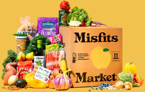A cardboard box with Misfits Market written on it and an assortment of fresh produce and packaged foods arranged around and on top of the box.