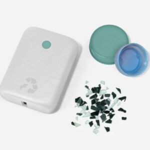 A small white portable charger with the recycling logo and a small elephant on it is shown next to two plastic bottle caps and shards of broken plastic.