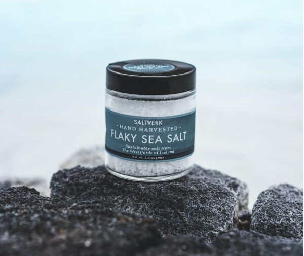 A jar of Saltverk’s flaky sea salt sits on top of a lava rock with a snowy Icelandic landscape out-of-focus in the background.