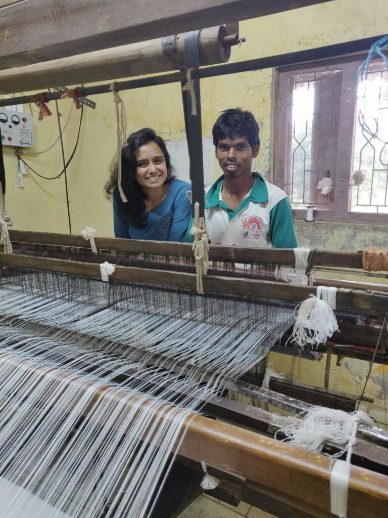 Founder of ReChakra sits behind a weaving machine with one of her employees 