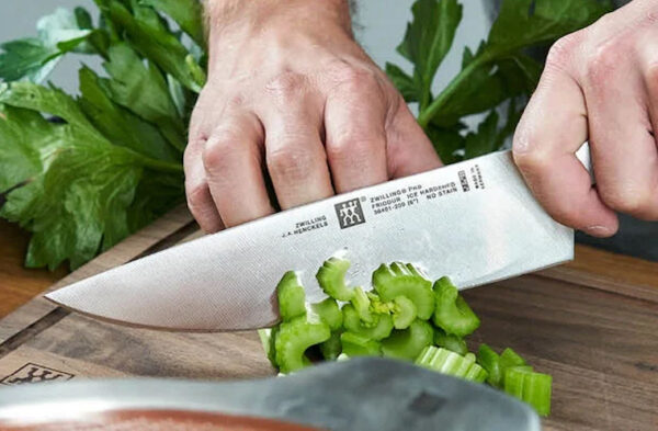 A close-up of a person chopping celery on a cutting board using a knife that's labeled Zwilling Pro.
