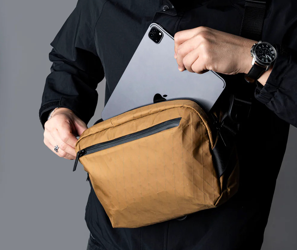 A close-up shot on a person putting a tablet into a camel-colored sling bag.