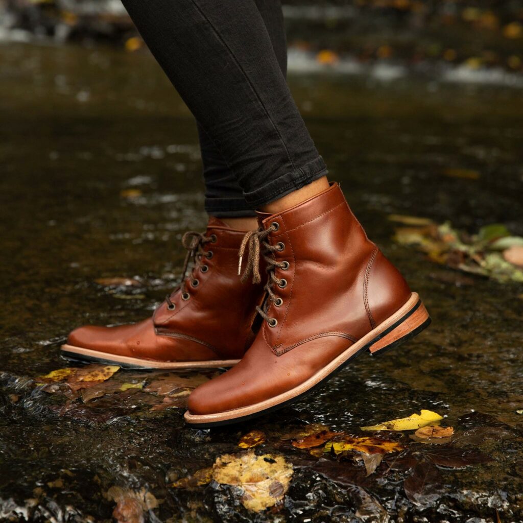 A pair of brown-leather, lace-up boots shown on someone wearing black pants, from mid-calf down.