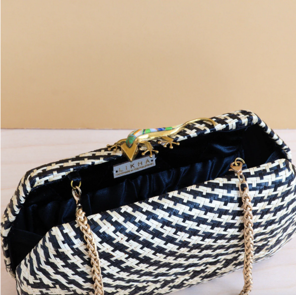 A small, woven purse in a black-and-white houndstooth pattern sits open. Its buckle resembles a small golden lizard. 