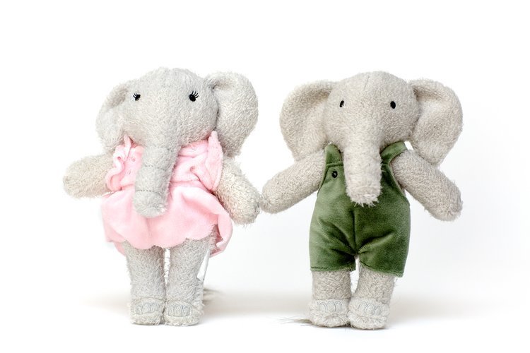 Two stuffed elephants, one wearing a pink dress and the other in a green romper. 