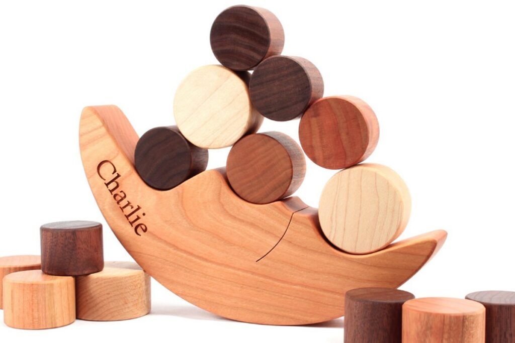 A crescent moon on its side, made from wood, with a smile and the name “Charlie” engraved on it, has round wooden circles balancing on top of it. 