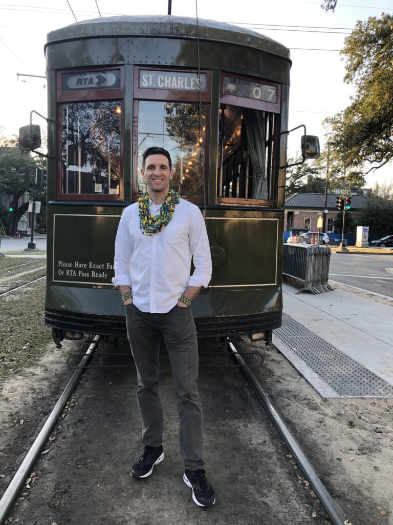 man standing in front of trolley in new orleans with bead necklace