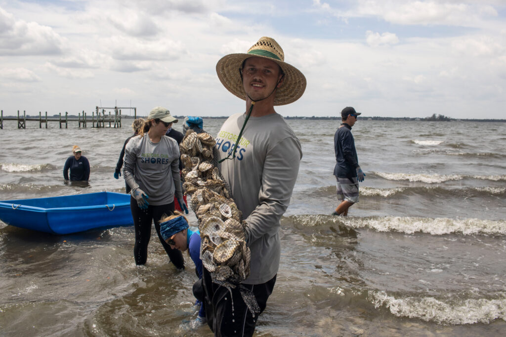 volunteer holding bag of oysters standing in shore