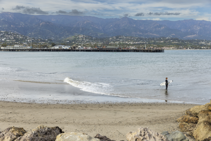 A person stands in the ocean with a surfboard by their side.
