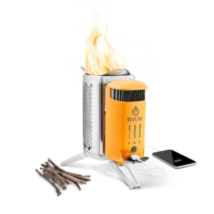 A small orange camp stove with the brand name BioLite on it is shown with flames coming out. Sticks rest on the side of the stove and a cell phone is plugged into the stove via USB cord.