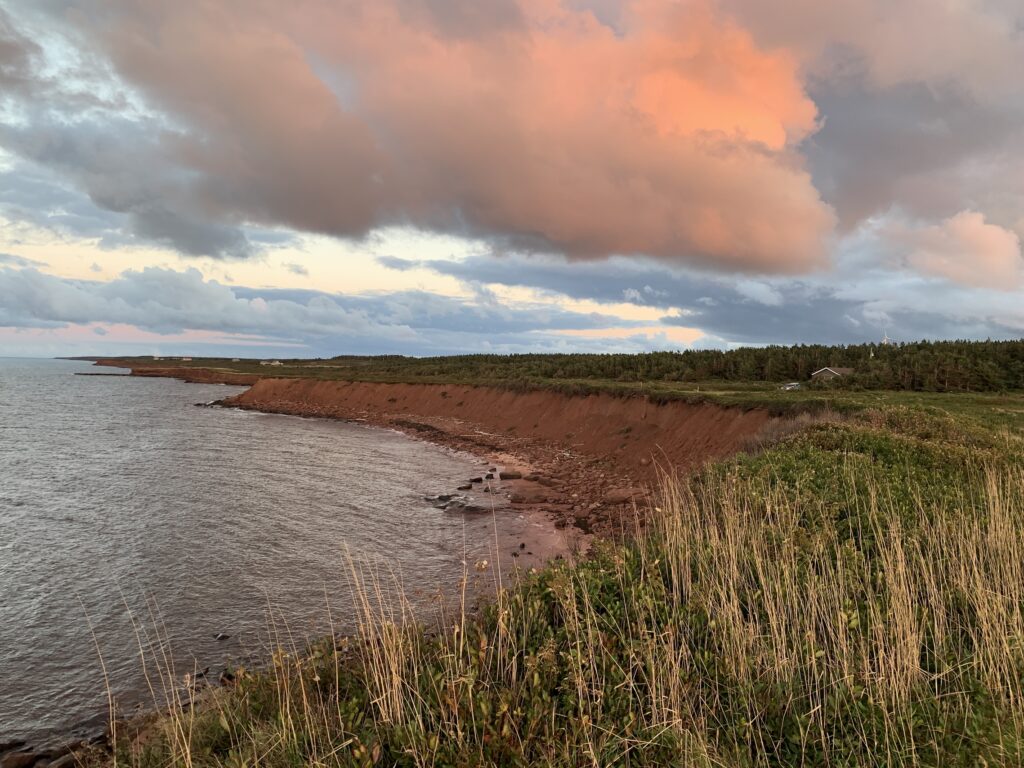red cliffs by body of water with pink clouds