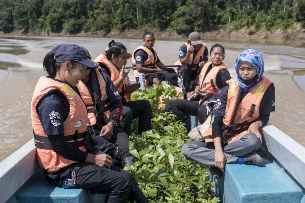 Team members on a boat with saplings by their feet.