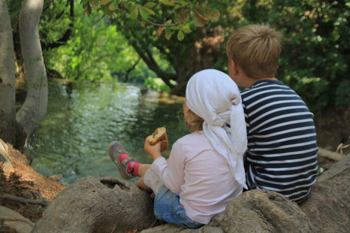 two children sitting on a rock by a wooded river