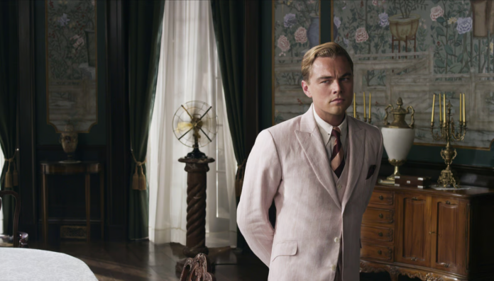 Leonardo Dicaprio, in the role of Jay Gatsby in the 2013 Warner Bros. film adaptation of the book, wears a pale pink striped linen suit while staring pensively in the middle of a grand room.