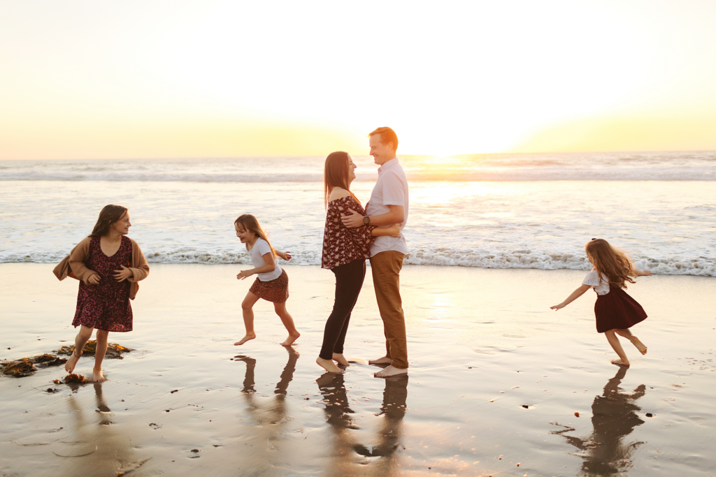 family on beach with children running around parents and sun setting