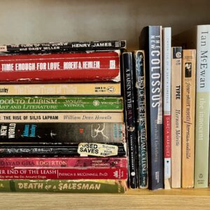 A shelf of about 30 heavily used books with creased spines, mostly fiction titles, with authors including Robert A. Heinlein, Aldous Huxley, Henry James, Arthur Miller, Marshall Goldberg, Herman Melville, Lorraine Hansberry, and more.