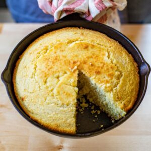 A large cast iron skillet with a cooked cornbread with one slice missing.