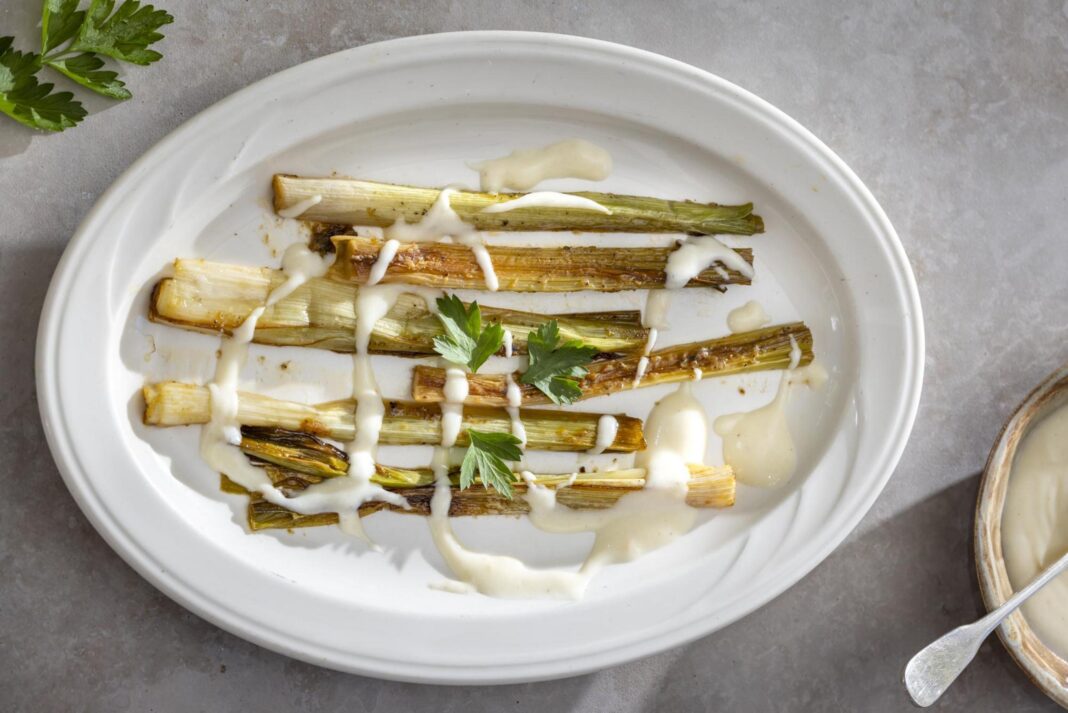 braised leeks on a plate with cheese sauce drizzled over them
