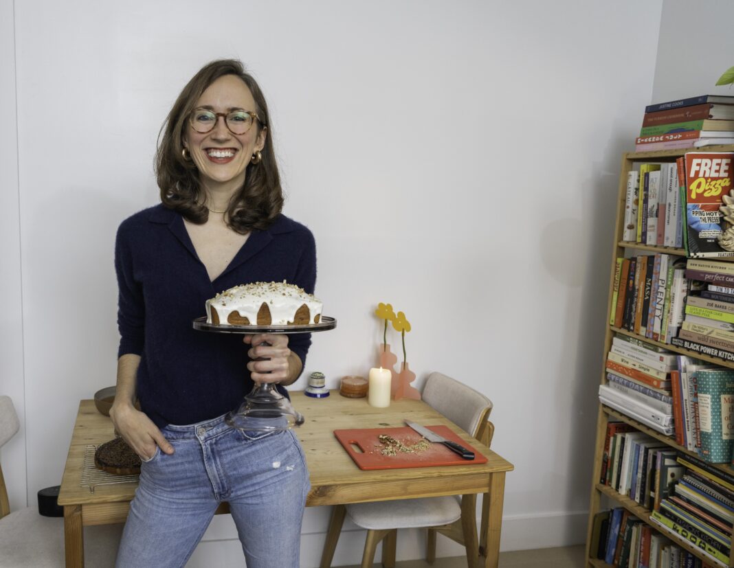 a woman standing in her apartment, holding a cake