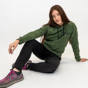 A woman with long reddish hair and freckles wears black plants and a stripey olive green hoodie with the brand name Coalatree.