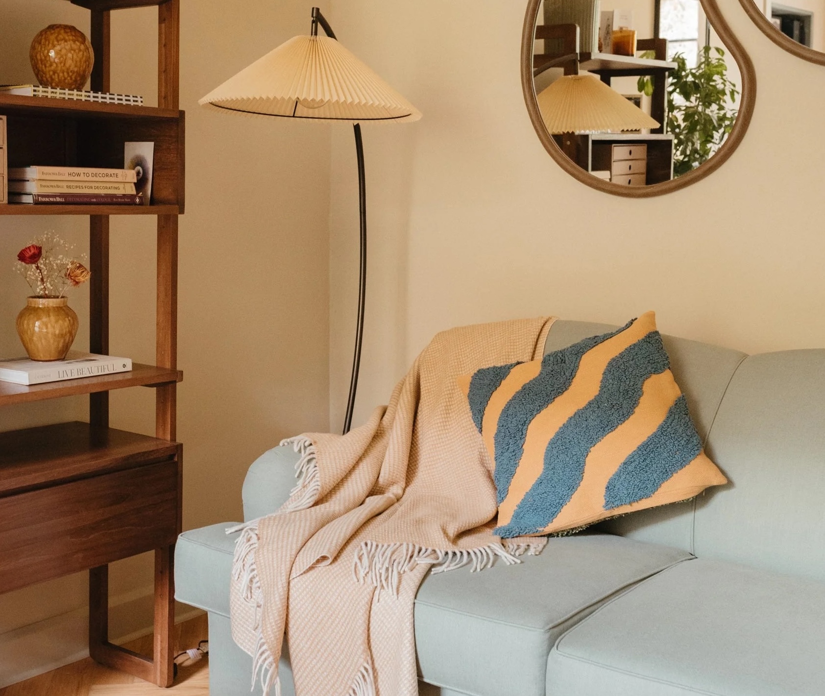 A contemporary room with a grey sofa with an orange tassled wool blanket and a gray and orange pillow on it.