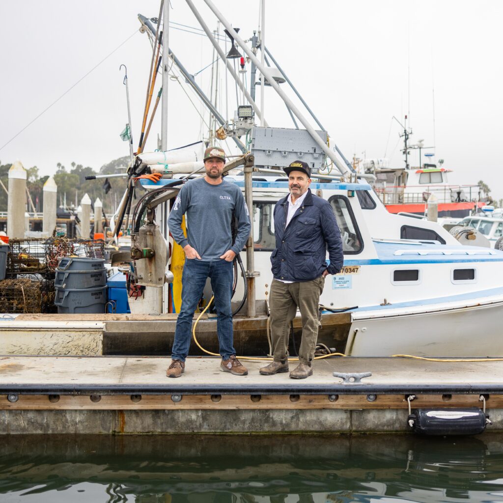 two men standing on a dock in front of a boat