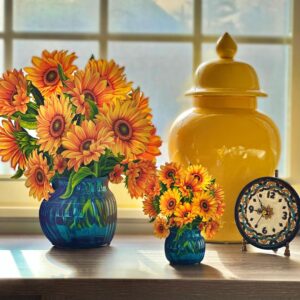 Two pop-up paper arrangements of sunflowers in blue vases, one small and one large, on a table in front of a window.