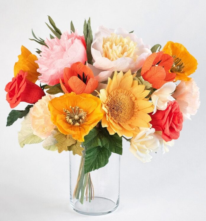 A bouquet of paper flowers in pink, orange, and yellow colors in a clear vase.