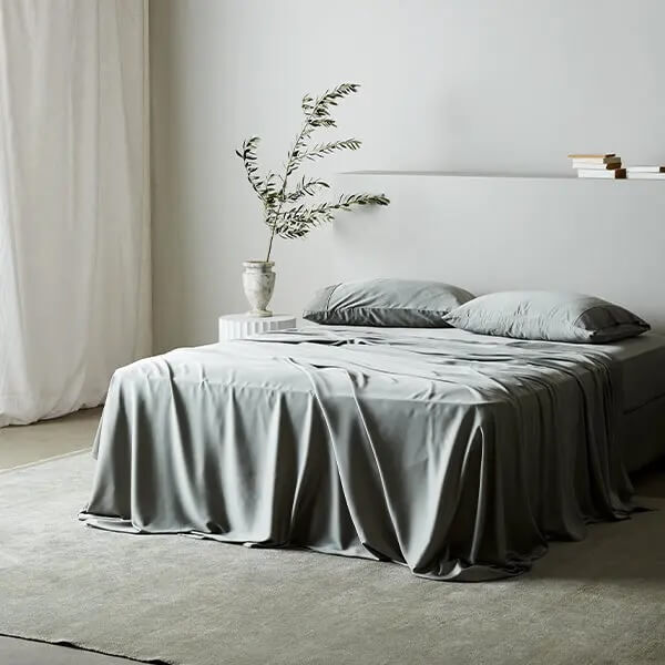 A bed made with shiny grey sheets.