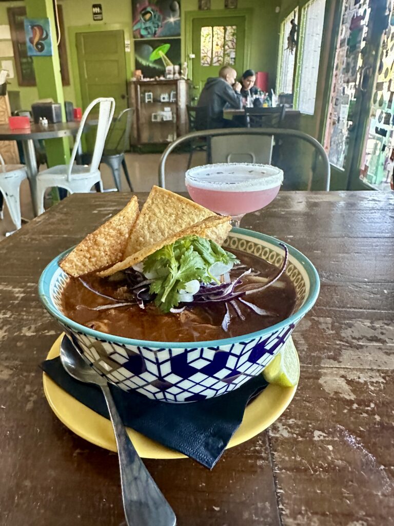 pozole in a bowl with tortilla chip garnish and drink in background