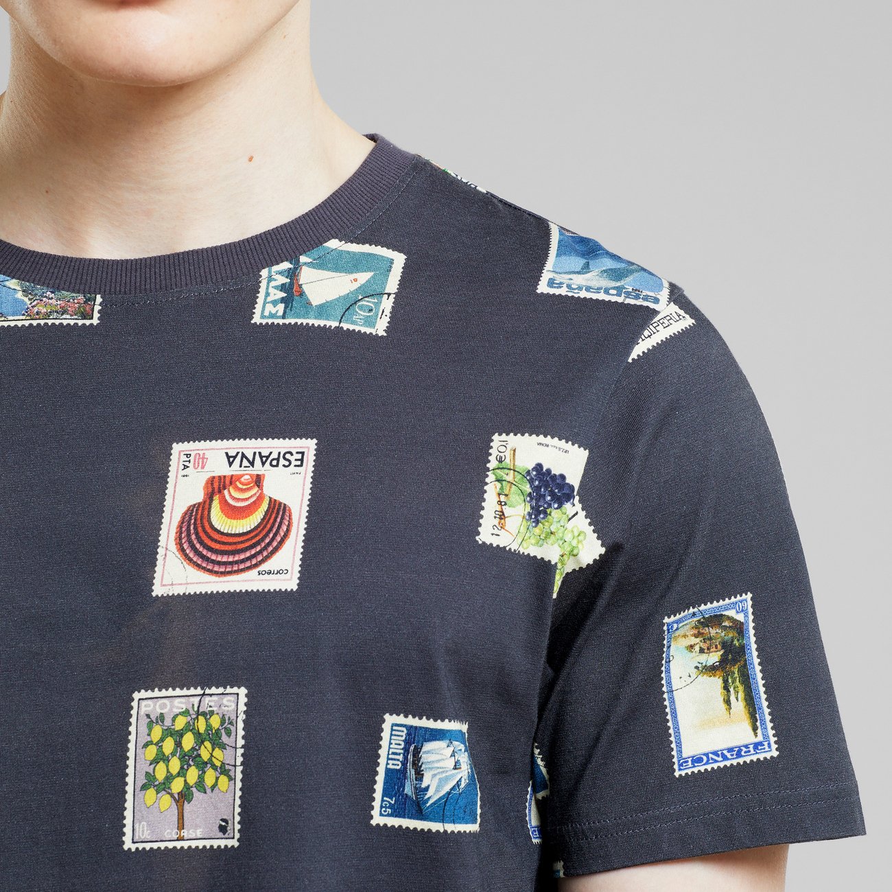 Close-up of a person in a navy T-shirt featuring a colorful postage stamp print design.