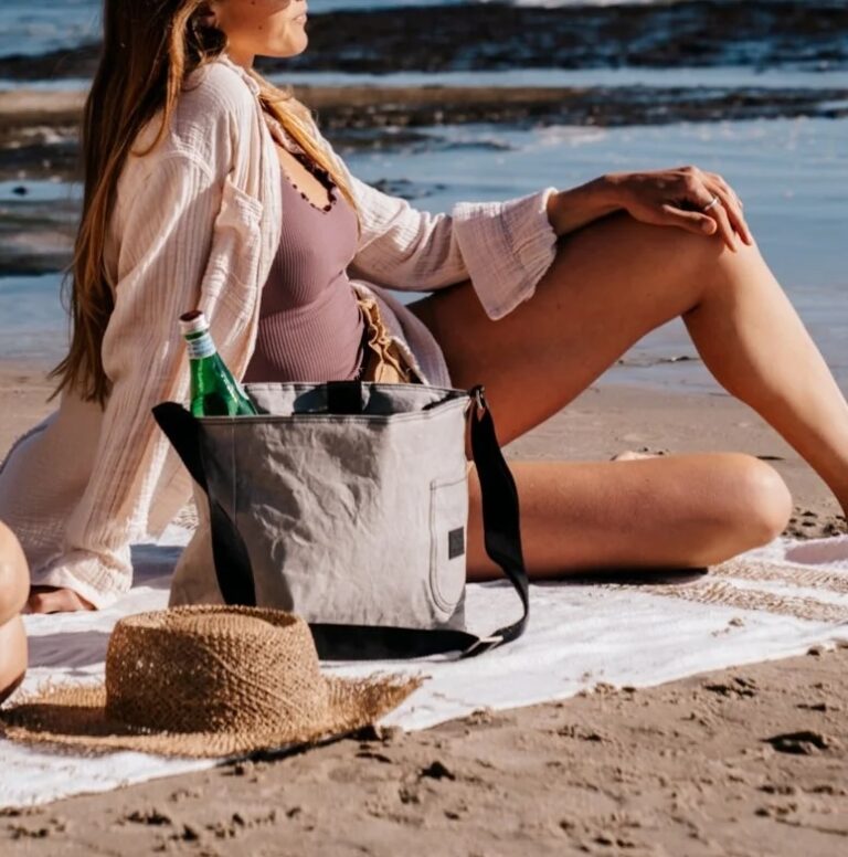 a person sits on a blanket on the beach next to a gray cooler
