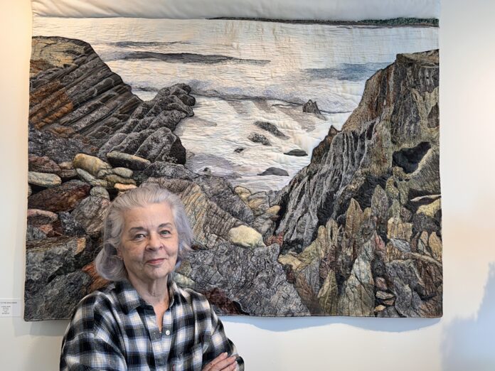 an artist stands in front of her handmade quilt